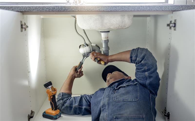 Plumber repairing pipes beneath a bathroom sink in Laguna Beach